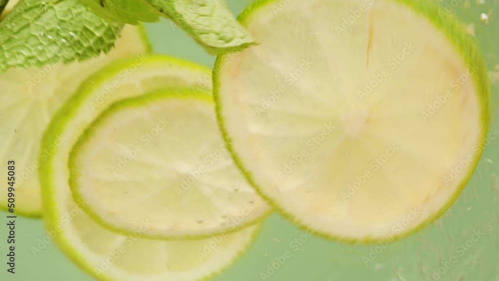 Lemon and lime cocktail, cooking cold lemonade, citrus fruits in water on green background, shooting of carbonated water with floating sliced fruits. Lemon and lime cocktail, cooking cold lemonade, citrus fruits in water on green background, shooting of carbonated water with floating sliced fruits.