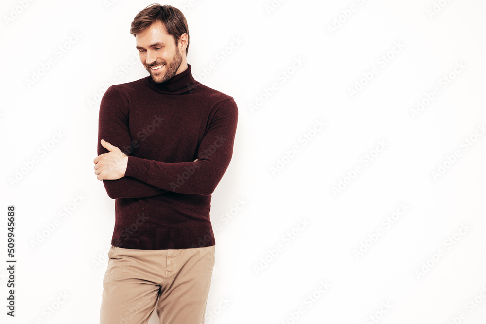 Portrait of handsome smiling stylish hipster lambersexual model. Sexy man dressed in turtleneck sweater and trousers. Fashion male isolated on white wall in studio. Crossed arms Portrait of handsome smiling stylish hipster lambersexual model. Sexy man dressed in turtleneck sweater and trousers. Fashion male isolated on white wall in studio. Crossed arms