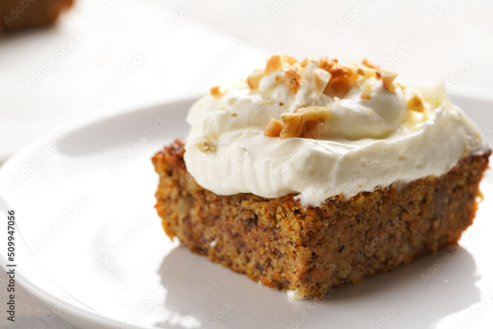 Homemade pastry carrot-walnut cake with grounded almonds and hazelnuts and white cream cheese top layer on white plate