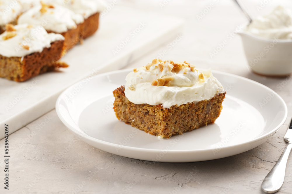 Homemade pastry carrot-walnut cake with grounded almonds and hazelnuts and white cream cheese top layer on white plate