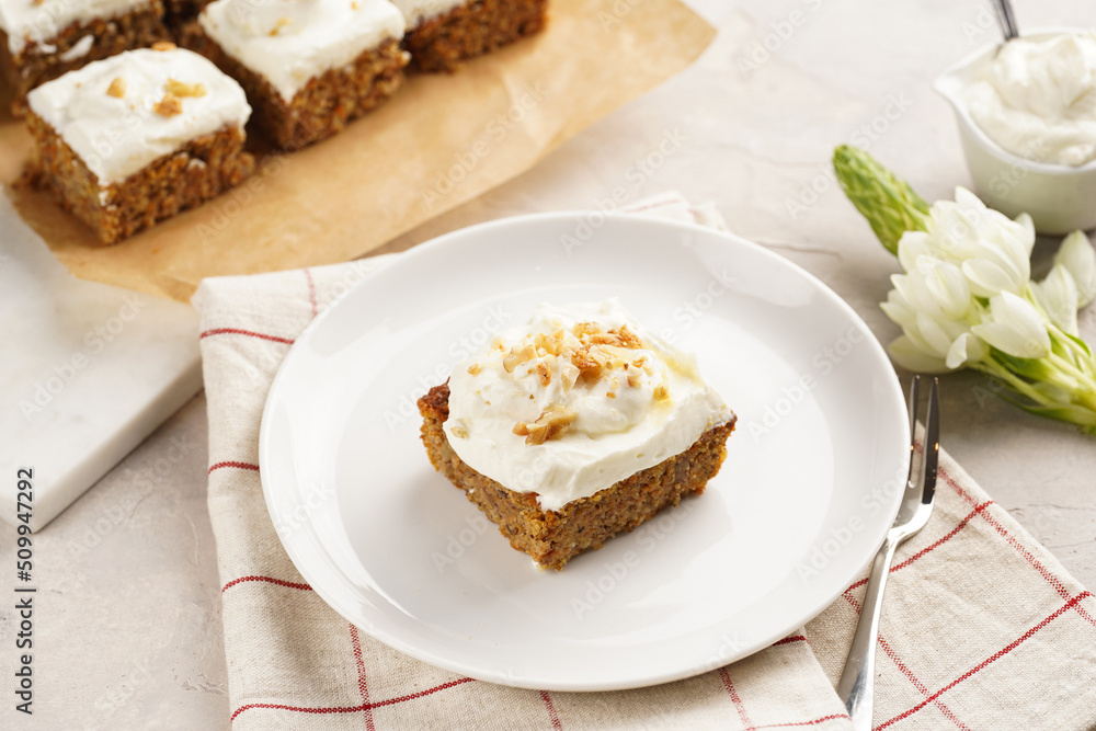 Homemade pastry carrot-walnut cake with grounded almonds and hazelnuts and white cream cheese top layer on white plate on pink checkered napkin Homemade pastry carrot-walnut cake with grounded almonds and hazelnuts and white cream cheese top layer on white plate on pink checkered napkin