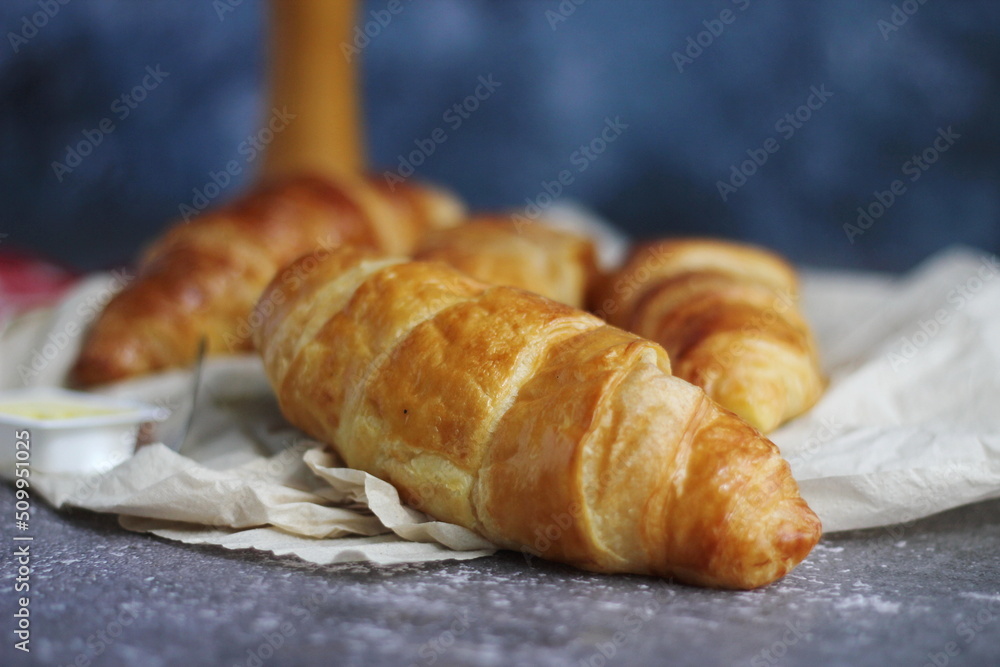 A pile of delicious fresh croissants served with butter. On a gray table with a blue background.