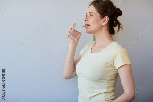 Smiling woman drinking water looking away. Girl in casual clothes isolated portrait.