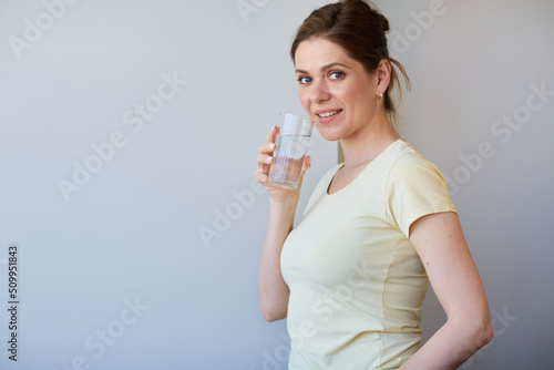 Smiling woman drinking water with glass, isolated head shot.