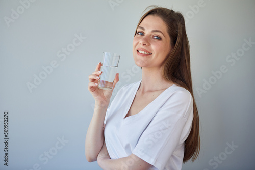 Smiling woman holding water glass. isolated portrait of girl wearing white shirt.
