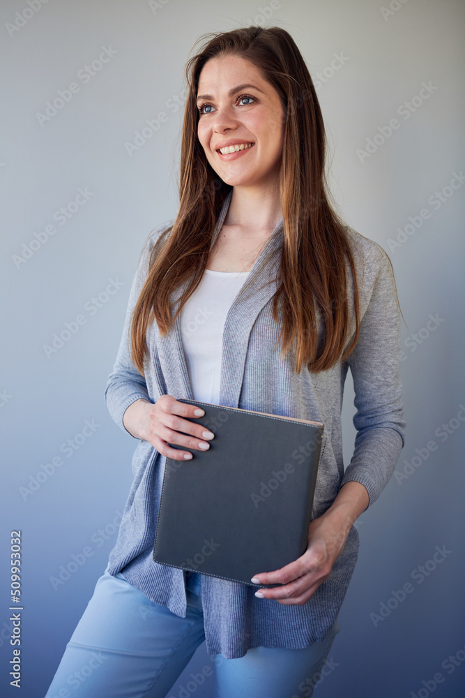 Obraz premium Smiling student or woman teacher wearing cassual holding book looking away. Isolated portrait on gray.