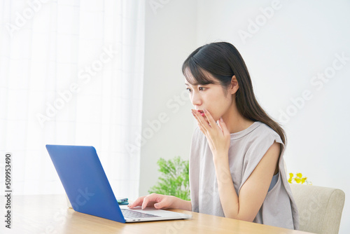 リビングでノートパソコンを見て驚く女性
