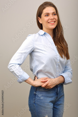 Smiling woman in blue shirt looking away and keeps her hands on hip. isolated portrait.