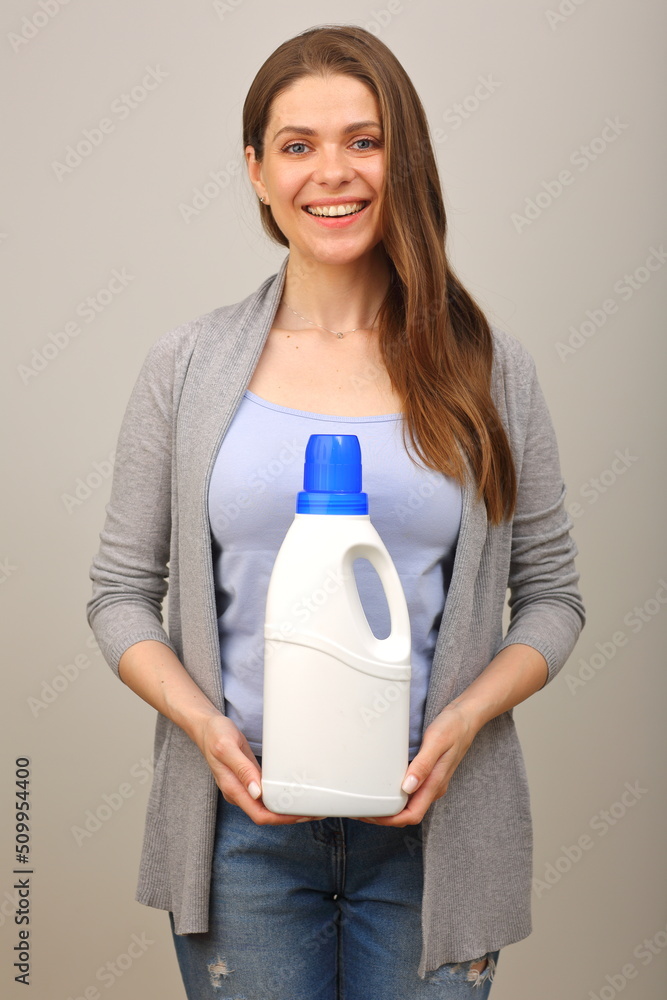 Young woman with long brown hair in casual clothes holding laundry detergent. Isolated portrait on gray. Young woman with long brown hair in casual clothes holding laundry detergent. Isolated portrait on gray.