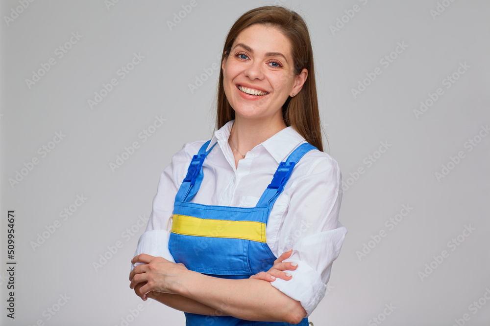 Smiling woman in blue overall uniform and white shirt standing with crossed arms. Isolated portrait of girl student vocational school.