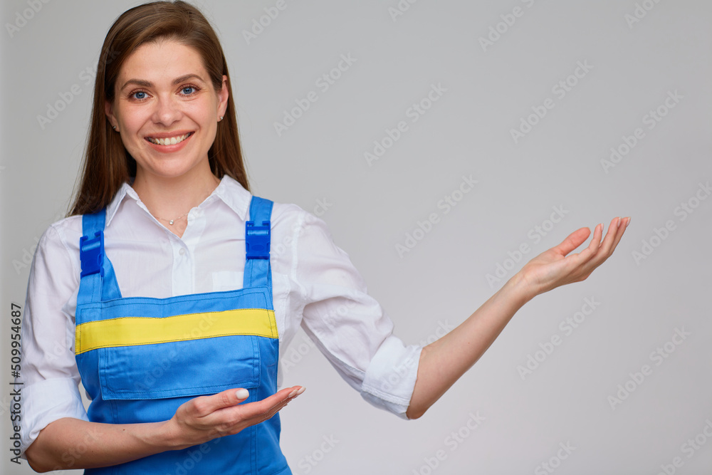Smiling woman in blue overall uniform and white shirt pointing with two hands at empty space. Smiling woman in blue overall uniform and white shirt pointing with two hands at empty space.