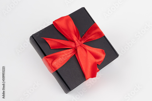 Free floating black gift box with red ribbon isolated on white. Holiday concept
