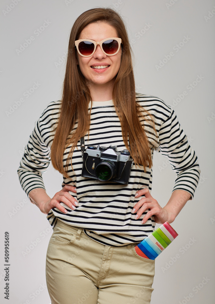 Woman in striped shirt with photo camera keeps hands on hip. Girl portrait on isolated gray background. Pssport in pants pocket. Woman in striped shirt with photo camera keeps hands on hip. Girl portrait on isolated gray background. Pssport in pants pocket.