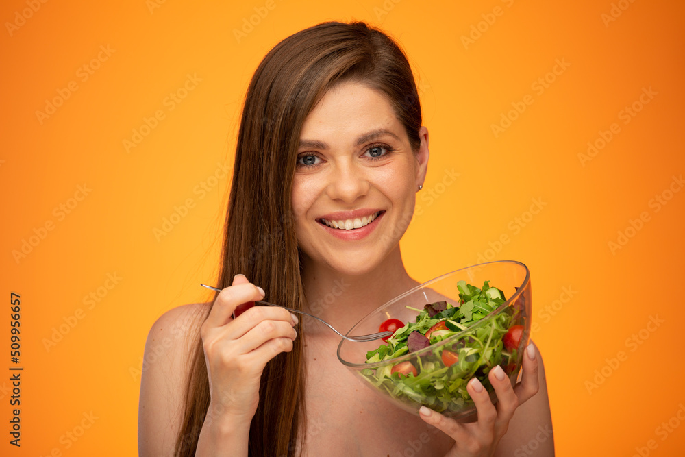 Smiling woman with naked shoulders holding bowl with green salad isolated on orange yellow background. Smiling woman with naked shoulders holding bowl with green salad isolated on orange yellow background.