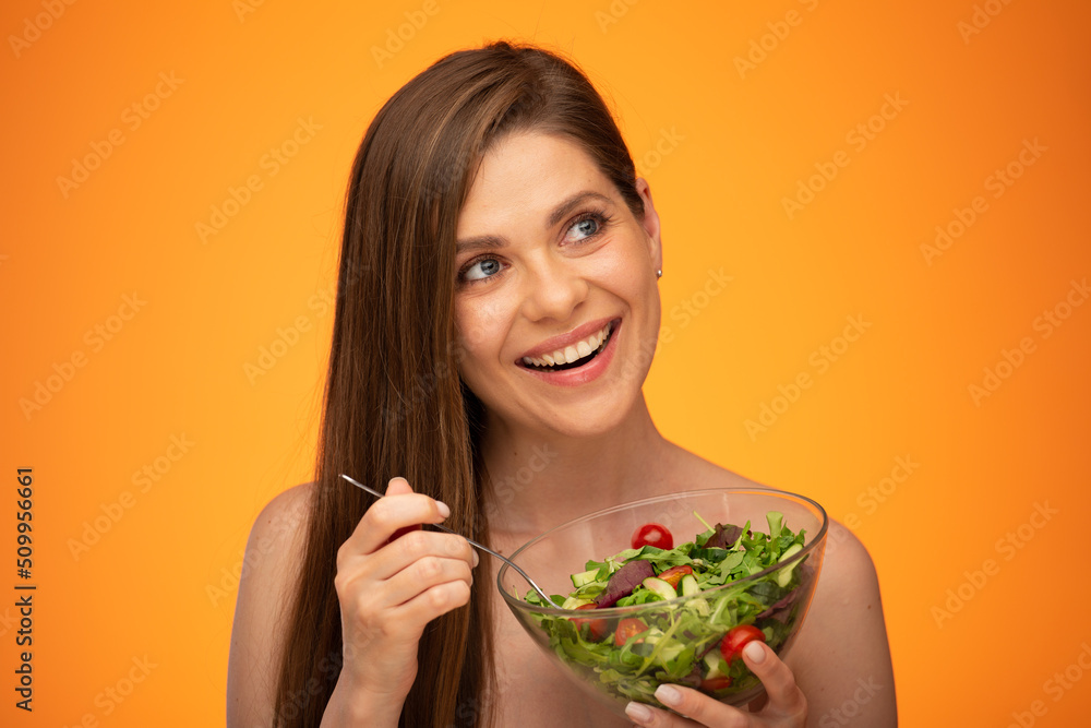 Laughing woman with bared shoulders holding green salad in glass bowl and looking away isolated portrait over orange yellow background. Laughing woman with bared shoulders holding green salad in glass bowl and looking away isolated portrait over orange yellow background.