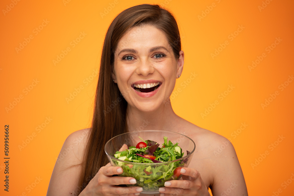 Happy woman with bare shoulders and long hair holding bowl with green salad and tomatoes isolated on orange yellow background. Happy woman with bare shoulders and long hair holding bowl with green salad and tomatoes isolated on orange yellow background.