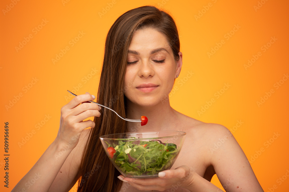 Happy dreaming woman eating salad with closed eyes, girl with bared shoulders and long hair isolated portrait on orange yellow background. Happy dreaming woman eating salad with closed eyes, girl with bared shoulders and long hair isolated portrait on orange yellow background.