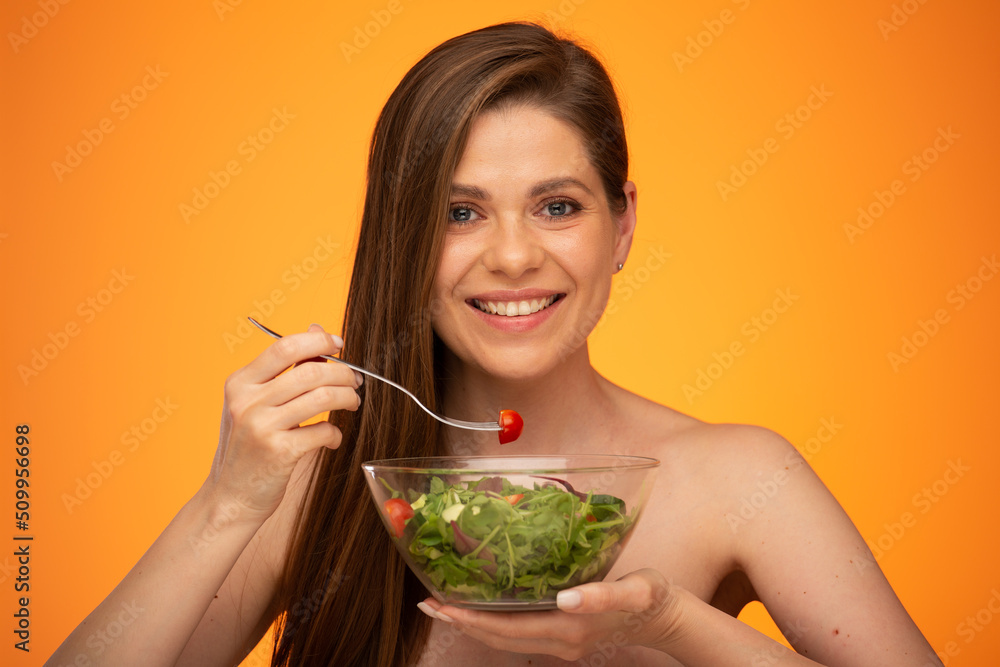 Woman with bare shoulders eating green salad isolated portrait on orange yellow background. Woman with bare shoulders eating green salad isolated portrait on orange yellow background.