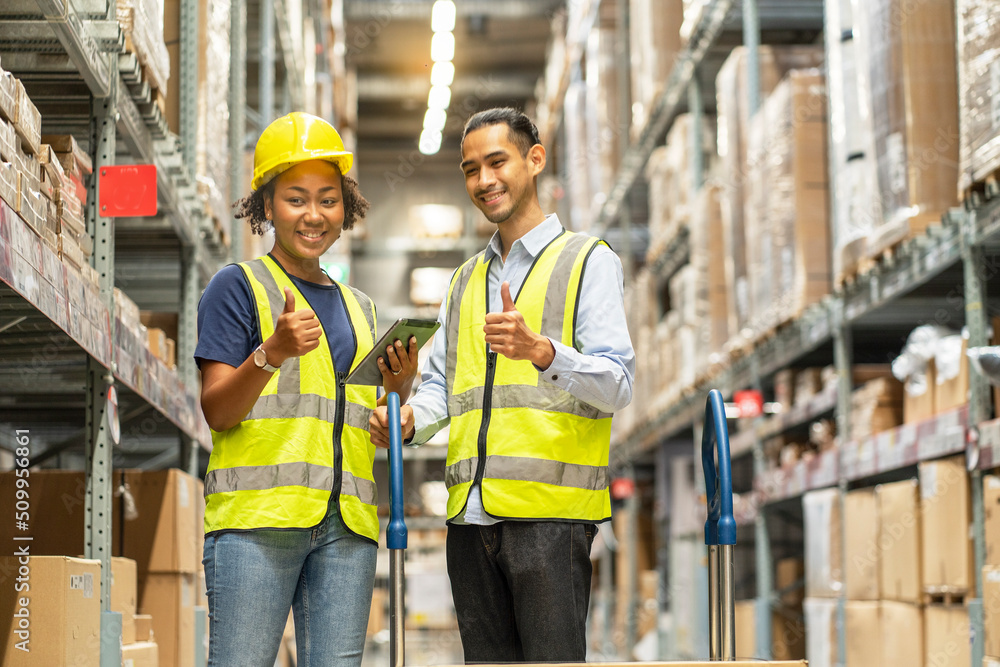 African American female worker and an Asian male worker wearing a uniform use their hands to collide with each other to complete a product inspection at warehouse African American female worker and an Asian male worker wearing a uniform use their hands to collide with each other to complete a product inspection at warehouse