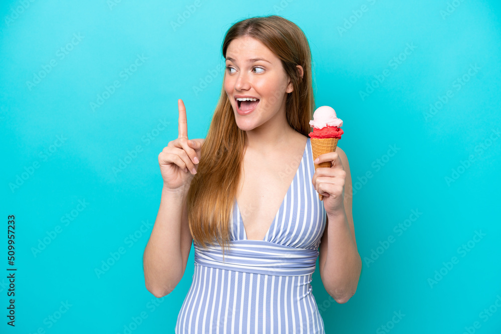 Young caucasian woman in swimsuit eating ice cream isolated on blue background intending to realizes the solution while lifting a finger up Young caucasian woman in swimsuit eating ice cream isolated on blue background intending to realizes the solution while lifting a finger up