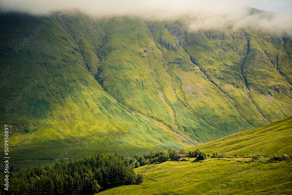 View of a ragged mountain slope covered in grass with low clouds in Glen coe, Scottish Highlands, UK