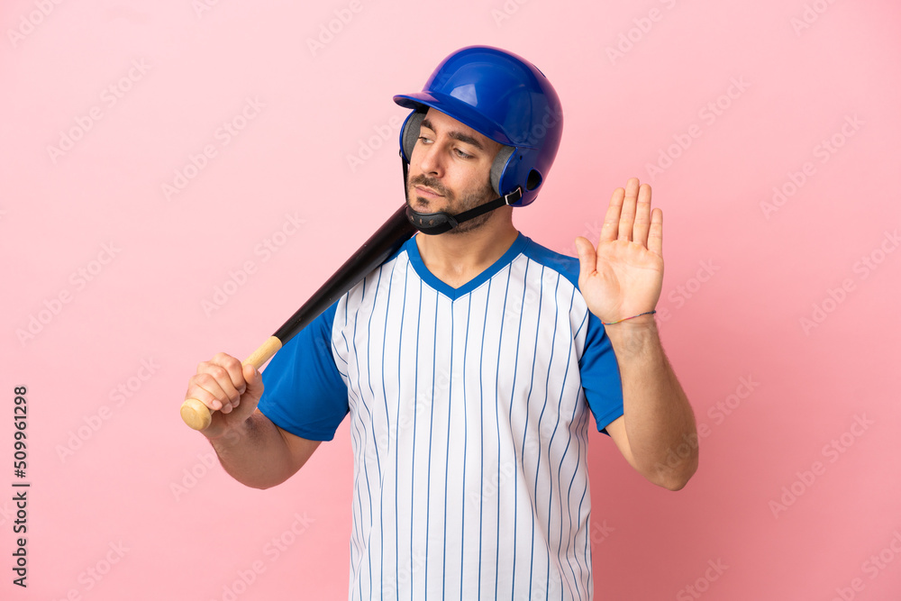 Baseball player with helmet and bat isolated on pink background making stop gesture and disappointed