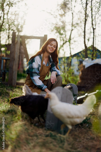 A beautiful woman works on a farm and pours fresh food from a bowl and feeds the chickens and makes sure the food is clean and organic for the health of the faces and chickens on a summer sunny day