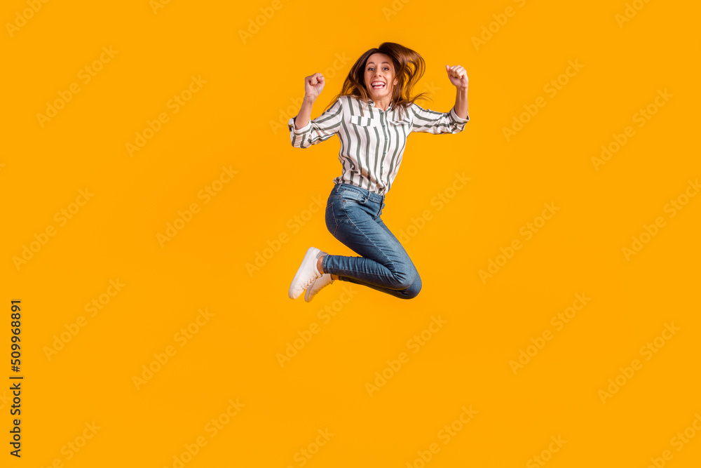 Full body profile side photo of young woman jumper rejoice success fists hands isolated over yellow color background Full body profile side photo of young woman jumper rejoice success fists hands isolated over yellow color background