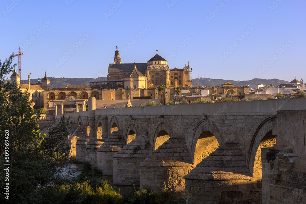 The first sunrays shine through the arches of the ancient roman stone bridge over the Guadalquivir river in the morning hours, Cordoba, Spain