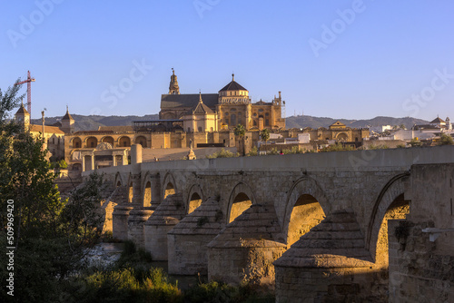 The first sunrays shine through the arches of the ancient roman stone bridge over the Guadalquivir river in the morning hours, Cordoba, Spain