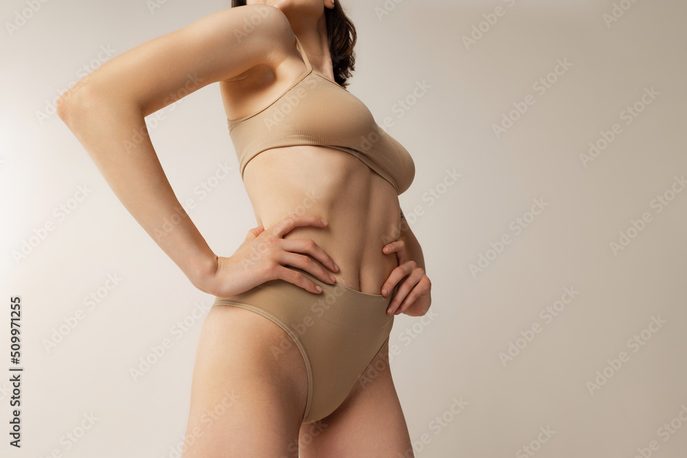 Cropped image of slim female body in beige underwear isolated over grey studio background. Sportive waist