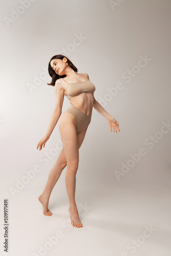 Portrait of beautiful young woman posing in beige underwear isolated over grey studio background. Natural beauty