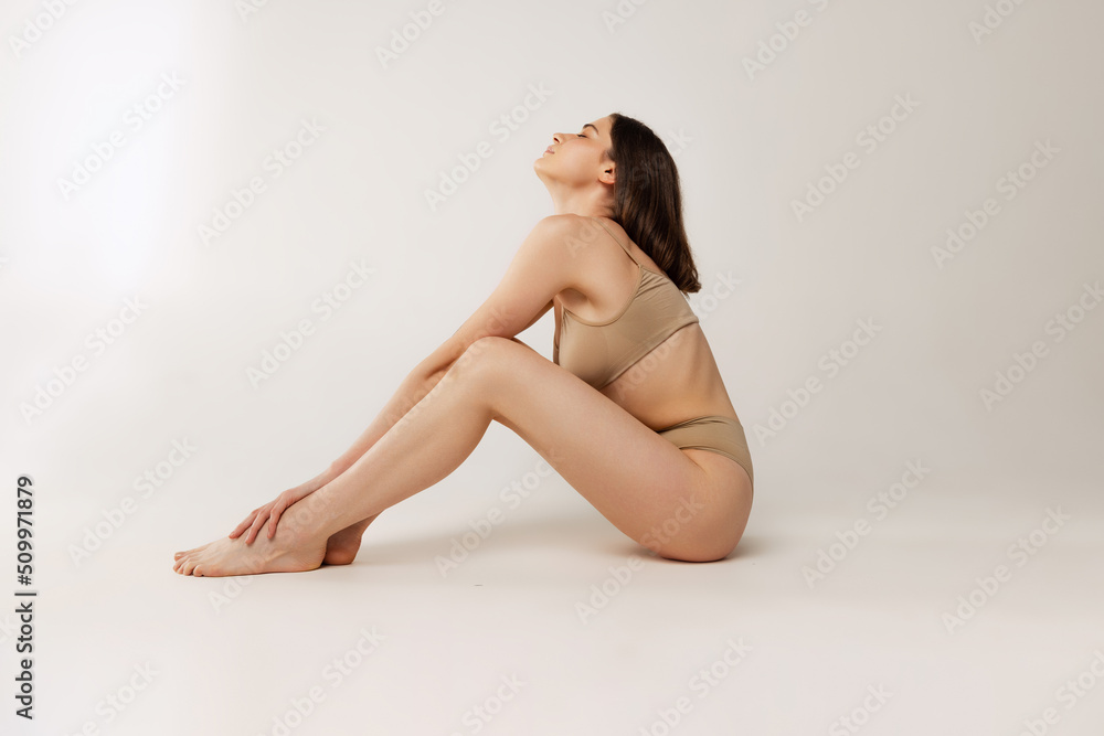 One beautiful young woman sitting on floor, posing in cotton beige underwear isolated over grey studio background. Comfort One beautiful young woman sitting on floor, posing in cotton beige underwear isolated over grey studio background. Comfort