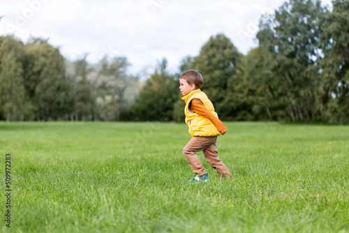childhood, leisure and people concept - happy little boy running on green field at park
