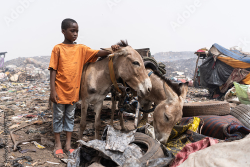 Lonely small African boy standing with garbage carrying donkeys posing on a huge waste dump in the African capital Bamako, in Mali. photo