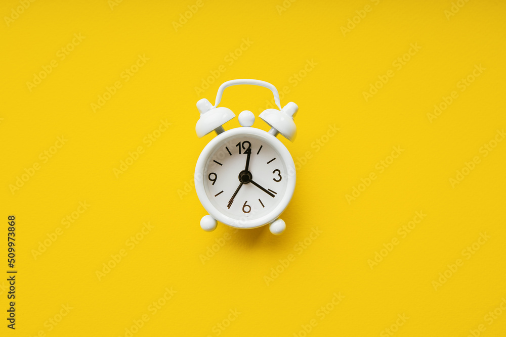 White alarm clock isolated on a yellow paper background. Deadline concept White alarm clock isolated on a yellow paper background. Deadline concept