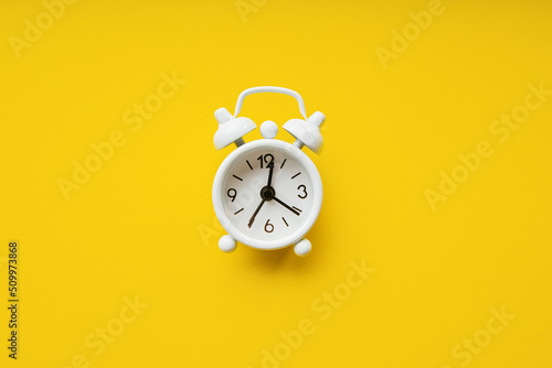 White alarm clock isolated on a yellow paper background. Deadline concept