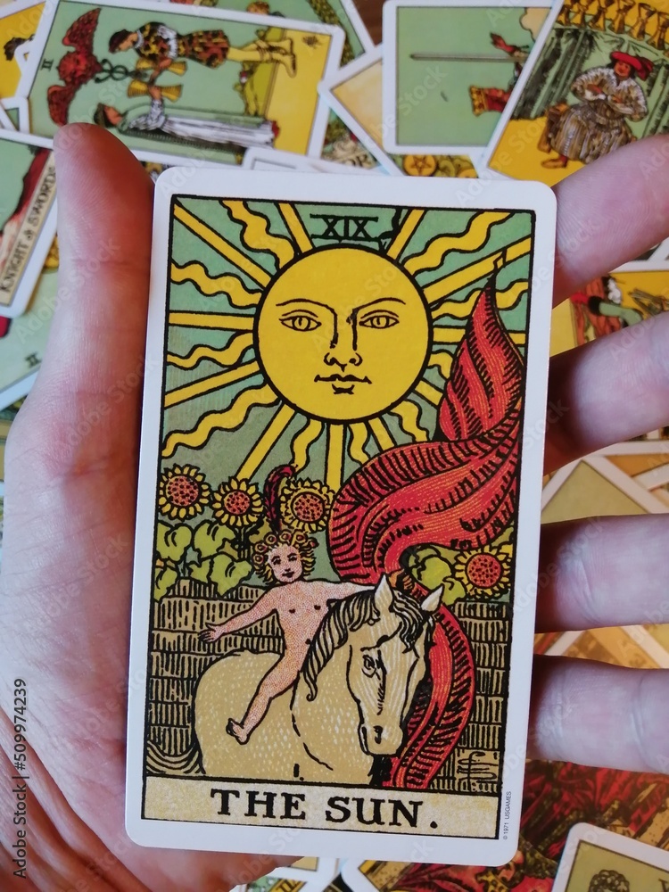 Picture of The Sun tarot card held in hand from the original Ride Waite  tarot deck with mixed tarot cards in the background Photos | Adobe Stock