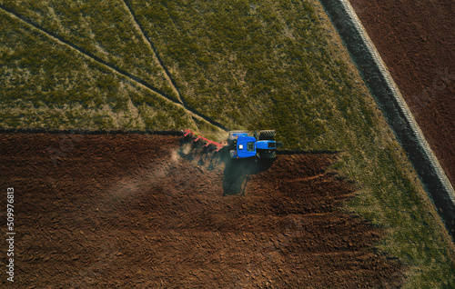Aerial view of a tractor plowing a field by tilling the soil with a mechanized plow ahead of the sowing period in Lomellina, Po Valley, Italy.