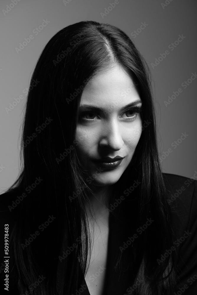 Fashion concept. Beautiful woman with dark hair and lipstick in dark lighting black and white studio portrait. Model looking aside the camera and wearing black classic suit. Part of face is in shadow