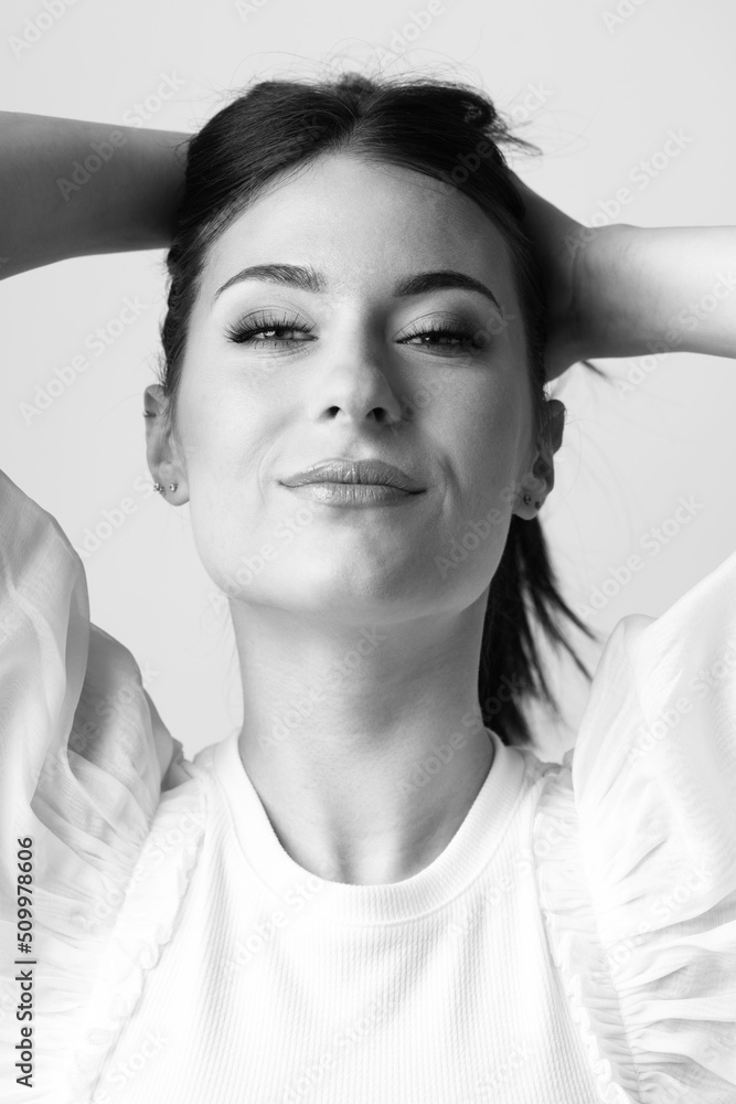 Beauty and lifestyle concept. Happy beautiful woman with dark hairs and day make-up close-up studio black and white portrait with hands behind her head and smile with happiness in her face Beauty and lifestyle concept. Happy beautiful woman with dark hairs and day make-up close-up studio black and white portrait with hands behind her head and smile with happiness in her face