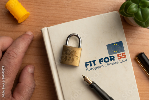 Fit for 55 european climate law concept: a book on a wooden table with a man hand a lock and a pen photo