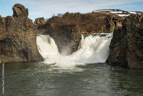 The picturesque Hjálparfoss waterfall in Þjórsárdalur valley, Iceland. The divided waters of river Fossá flow together in a beautiful basin lined by basalt rock formations.