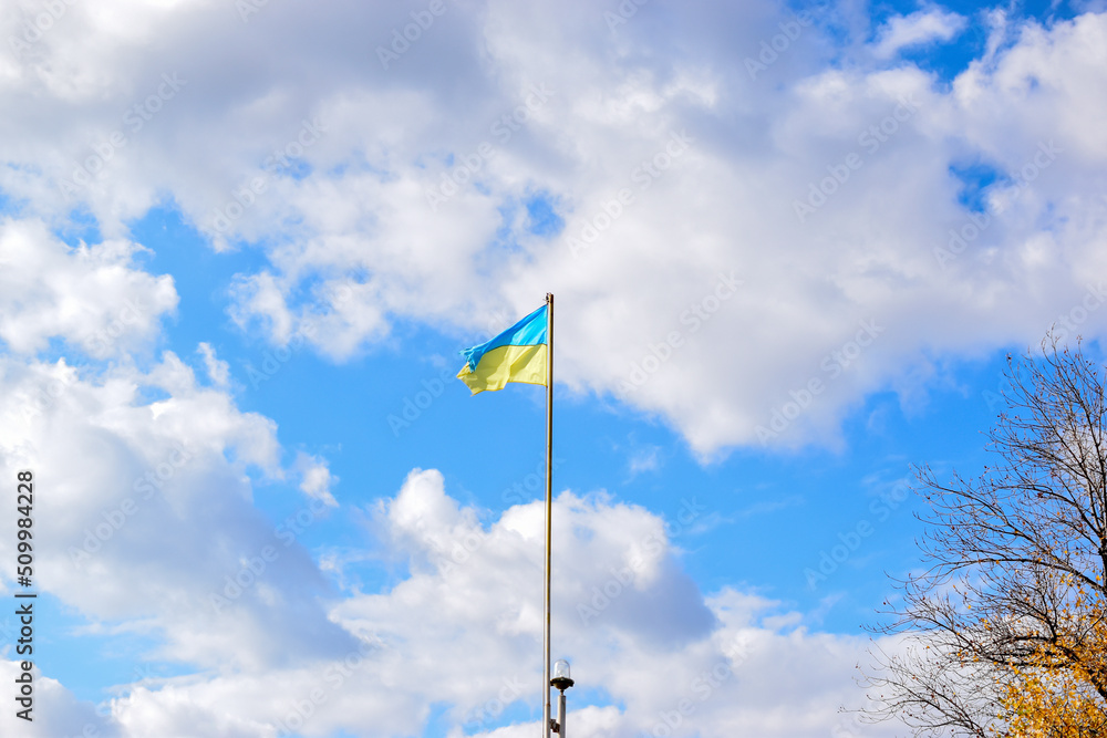 Flag of Ukraine on a long flagpole against a blue sky with white clouds