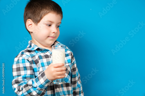 A 4-year-old boy holds a glass of milk and squirms looking into the camera. Cow's milk protein allergy, lactose intolerance, space for text.