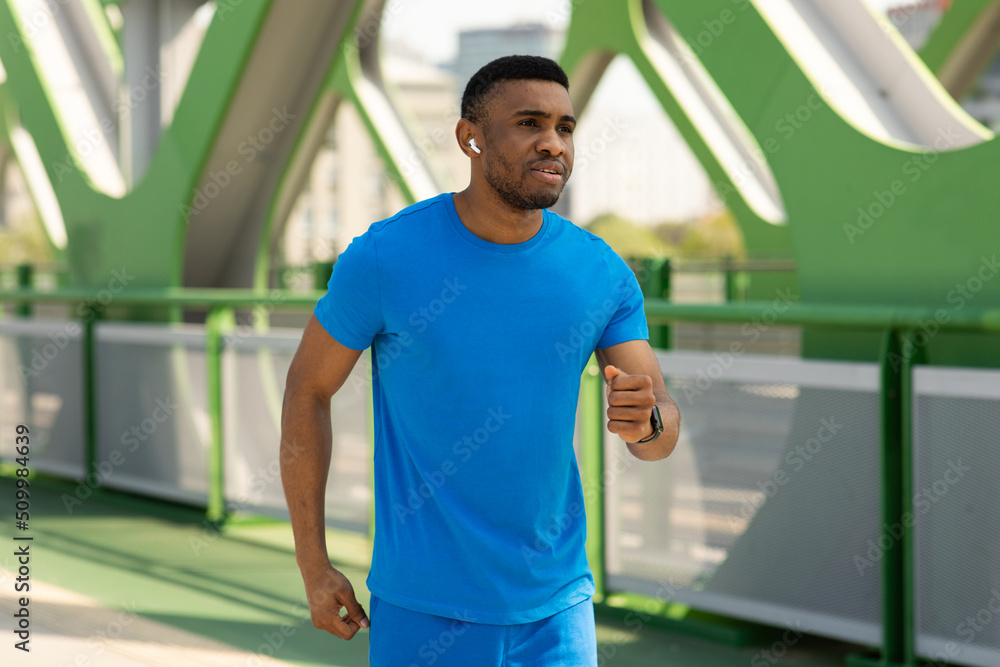Handsome young sportsman in blue t-shirt during intense cardio workout on hot summer day