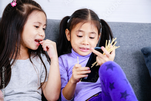 Two happy cute little girls playing game on smartphone together at home