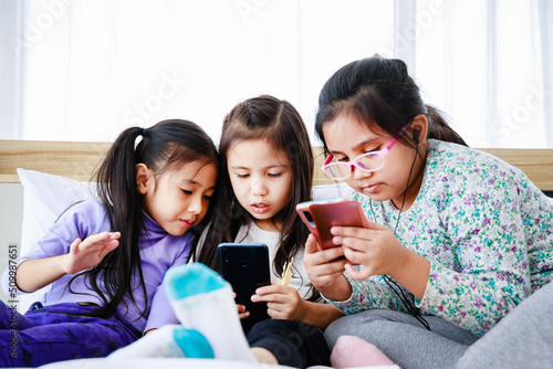 Three little girls playing smartphone for playing or studying together at home