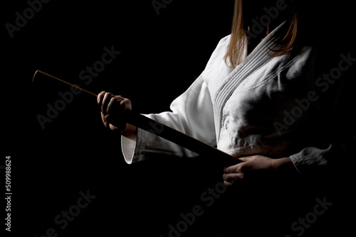 A girl in black hakama standing in fighting pose with wooden sword bokken over dark background. Shallow depth of field. SDF. 