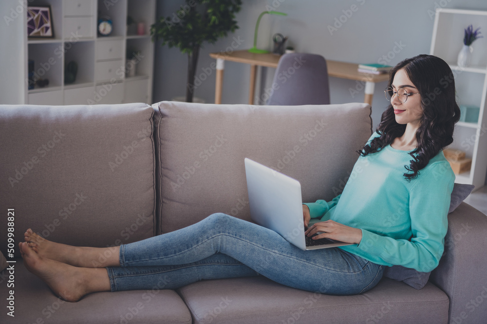 Full size profile side photo of young woman agent manager sit divan use laptop self isolation indoors Full size profile side photo of young woman agent manager sit divan use laptop self isolation indoors